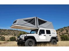 a jeep with a tent attached to it's roof in the middle of a field