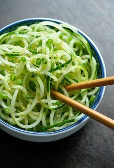 a bowl filled with cucumber noodles and chopsticks on top of a table