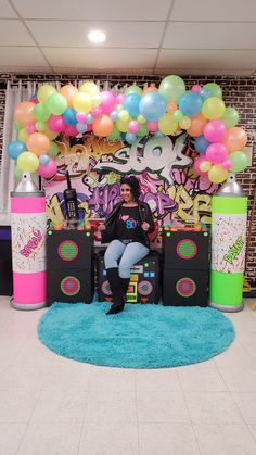 a woman sitting on a chair in front of a backdrop with balloons and music equipment