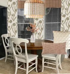 a dining room table with four chairs and a vase on top of it, in front of two windows