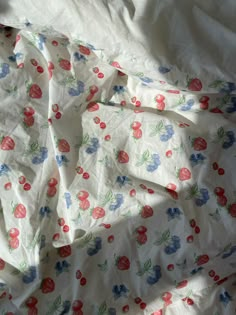 an unmade bed covered with white sheets and red, blue, and green flowers