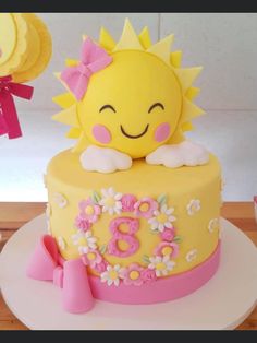 there is a yellow cake with pink decorations on the top, and a sun decoration on the bottom