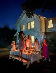 children are gathered around a table with food on it in front of a house at night