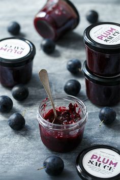 blueberries and plum jam in small jars with spoons on the table next to them