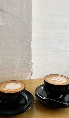 two cups of coffee sitting on top of a wooden table