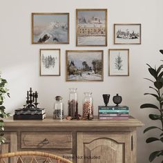 three framed pictures hang on the wall above a table with books, plants and vases