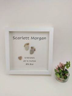 a white frame holds two small rocks and a vase with pink flowers on the side