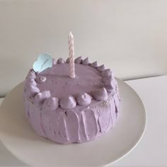 a birthday cake with purple frosting and a single candle on top is sitting on a white plate