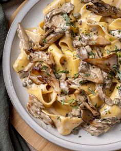 a white plate topped with pasta covered in mushrooms and sauce on top of a wooden cutting board