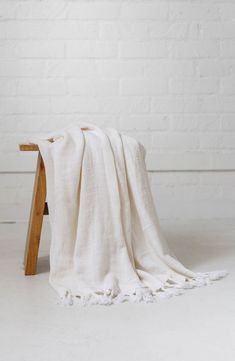 a white blanket sitting on top of a wooden stool next to a brick wall and floor