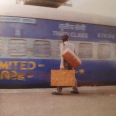 a man carrying two suitcases walking next to a train