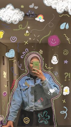 a woman taking a selfie in front of a mirror with colorful drawings on it