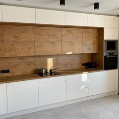 an empty kitchen with white cabinets and wood paneling on the back wall, along with black appliances