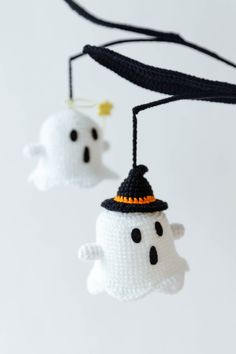 two crocheted ghost ornaments hanging from strings on a white background with black string