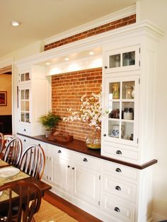 a dining room table and chairs in front of a brick wall with white cupboards