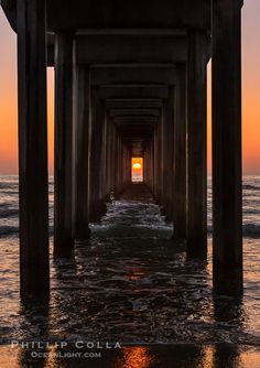 the sun is setting at the end of a long pier with water under it and waves coming in