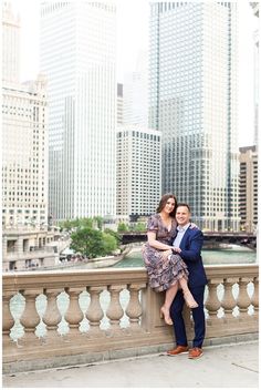 an engaged couple standing on a bridge in front of the chicago river and skyscrapers