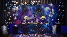 a space themed backdrop with balloons and flowers on the stage for a wedding or special event