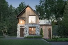 a small house is lit up in the evening with trees and bushes around it,