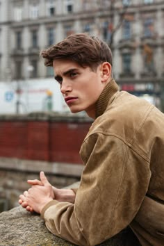 a young man sitting on top of a stone wall next to a train track and buildings