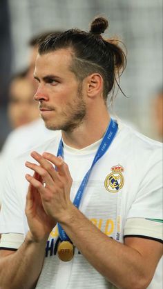 a male soccer player with a ponytail and medal around his neck looking to the side