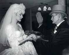 an old photo of a man and woman dressed up in wedding attire, one holding the bride's hand