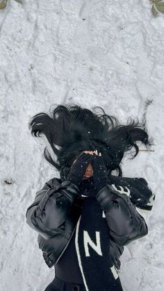 a woman laying in the snow with her hands on her face and hair blowing back