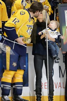 a man kissing a woman while holding a baby in front of an ice hockey team