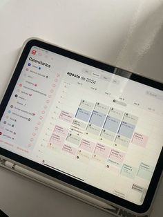 a tablet with a calendar on it sitting on top of a white table next to a cup