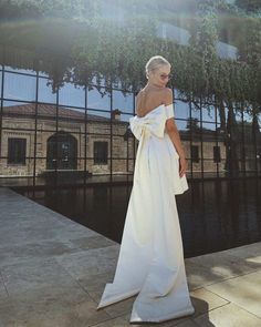 a woman in a white dress standing on the side of a building next to water