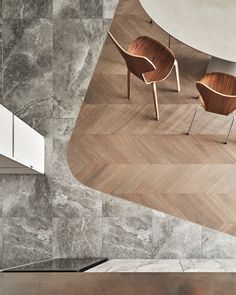 two chairs sitting on top of a wooden floor next to a wall with marble tiles