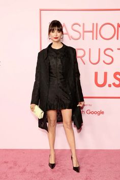 a woman standing on top of a pink carpet wearing a black dress and blazer