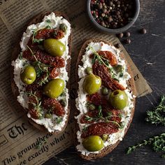 two pieces of bread with olives and cream cheese on it next to a bowl of pepper