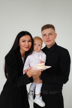 a man and woman holding a baby with a birthday cake on the plate in front of them