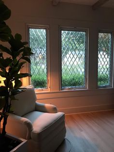 an empty living room with three windows and a white chair in the corner next to a potted plant