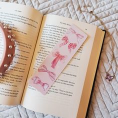 an open book with pink and white designs on it, sitting next to a necklace