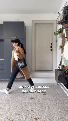 a woman walking across a kitchen floor holding a black handbag in her right hand