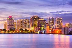 the city skyline is lit up at night with lights reflecting on the water and buildings in the background