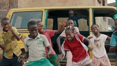 several children are dancing around in front of a yellow bus with their hands up and smiling