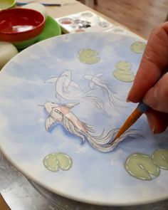 a person is drawing on a plate with water lilies and fish in the background