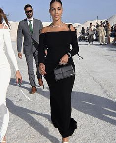 a woman in a black dress is walking down the street with other people behind her