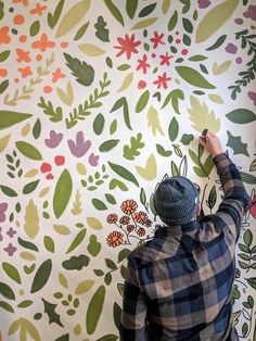 a man is painting a wall with flowers and leaves on the wall next to him