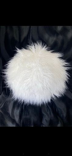 a white fur ball sitting on top of a black cloth