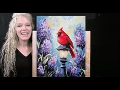 a woman standing next to a painting of a red bird on a street light with purple flowers