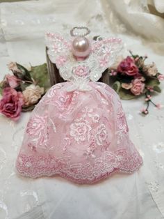 a pink dress with white lace and pearls on it sitting next to flowers in front of a mirror