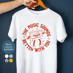 "Looking for a cool t-shirt for yourself or a gift for your best friend? Our \"The music sounds better with you\" retro inspired dancing cassette tape red tee is perfect for music concerts, festivals, or just because it's Tuesday. Grab your t-shirt today and let your unique style shine! HOW TO ORDER 1. Chose shirt colour Select from the drop down menu 2. Select shirt size See our size guide for details in the listings images 3. Add to cart Purchase your lovely new shirt SIZING AND COLOURS We offer inclusive sizing with our shirts, ranging from S-3XL. See our size guide for details in the listings images. We only offer colours that we know our designs will look great on. See our colour guide for options for this design in the listings images. PRODUCT DESCRIPTION A classic fit unisex t-shirt Cheap Music-themed T-shirt With Text Print, Cheap T-shirt With Sublimation Print For Music Festivals, White Graphic T-shirt For Music Festival, White Graphic Design T-shirt For Music Festival, White Music-themed T-shirt With Text Print, White Music-themed T-shirt For Fans, White Music-themed Fan Merchandise T-shirt, Music-themed White T-shirt With Graphic Design, Music-themed White Graphic T-shirt