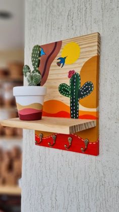 a potted cactus sitting on top of a wooden shelf next to a white wall