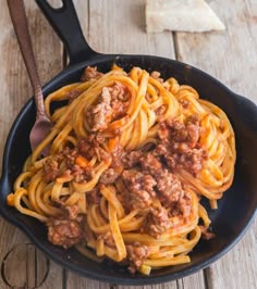 a skillet filled with spaghetti and meat sauce on top of a wooden table next to bread