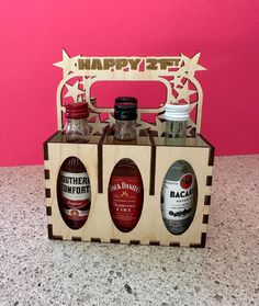 three bottles of booze sitting in a wooden crate on a countertop next to a pink wall