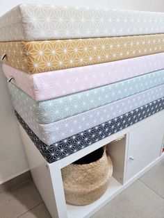 a stack of folded sheets sitting on top of a white shelf next to a basket